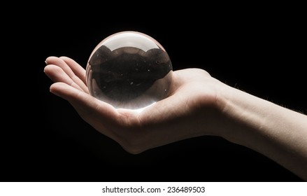 Hand Holding A Clear Transparent Crystal Glass Ball In Their Palm Isolated On Black Background