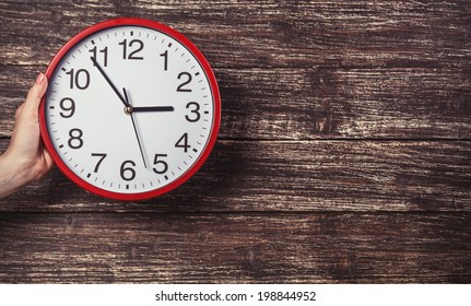 Hand Holding Clock On Wooden Background.