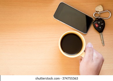 Hand holding coffee cup on wooden background, with phone and car key,top view.