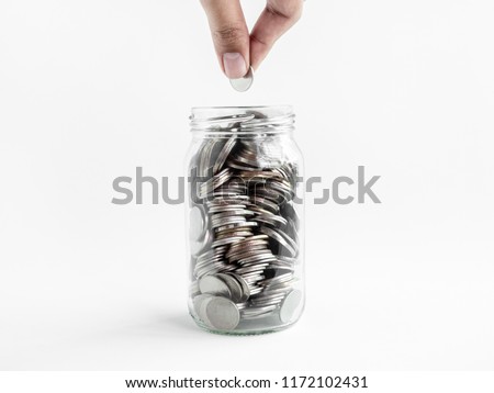 Hand holding coin in glass jar isolated on white background. Saving money concept.