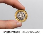 Hand holding a coin of one pound sterling close-up on a white background. UK currency.
