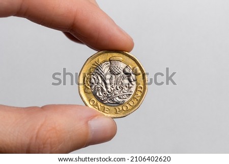Hand holding a coin of one pound sterling close-up on a white background. UK currency.
