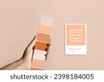 Hand holding Color samples palette design catalog. New trending PANTONE 13-1023 Peach Fuzz colour of 2024 year 