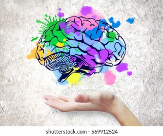 Hand holding colorful brain sketch on concrete background. Creative mind concept