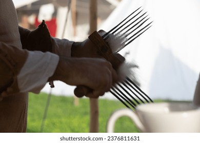 A hand holding a comb while combing wool fibers. The comb is used to separate and stretch the wool fibers - Powered by Shutterstock