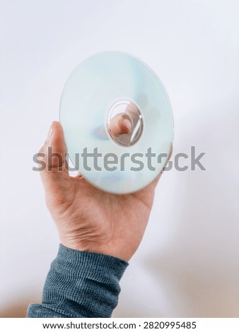 A hand holding a compact disc (CD) isolated on a white background. Ideal for concepts of digital storage, optical media, data backup, technology, music, software, and multimedia.