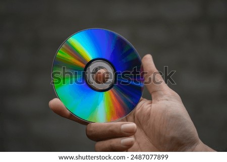 Hand holding a Compact Disk (CD) or Digital Versatile Disk (DVD) where digital data is stored with a blurred background