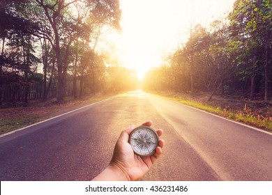 Hand Holding Compass On Empty Asphalt Road And Sunset.