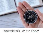 Hand holding compass on top of open holy bible book. Close-up. Guidance, instruction, Christian journey, following God Jesus Christ, biblical concept.