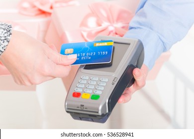 Hand Holding Contactless Credit Or Debit Card Over Wireless Payment Terminal At Shop With Gifts In The Background 