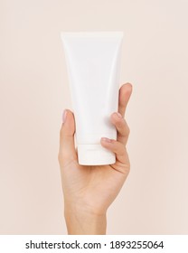 Hand Holding Cosmetic Plastic Tube Isolated On Beige Background.