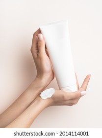 Hand Holding Cosmetic Plastic Tube Isolated On Beige Background. With White Cream Texture