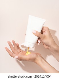 Hand Holding Cosmetic Plastic Tube Isolated On Beige Background. With Yellow Cream Texture