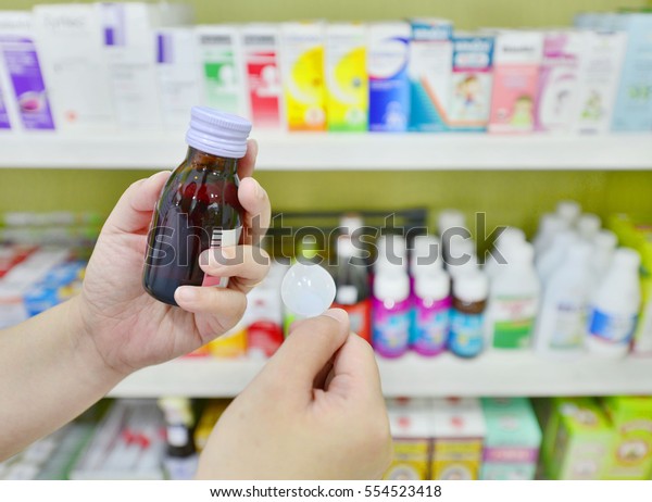 Hand\
holding a cough syrup bottle in pharmacy\
drugstore.