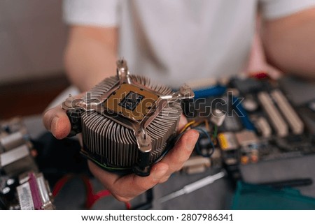 Hand holding CPU mounted on heatsink above computer motherboard, ready for installation or repair close-up of technician performing hardware maintenance and upgrade.