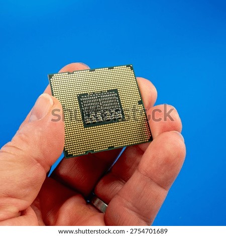 Hand holding a CPU processor showing the gold contact pins (LGA PGA socket side) against a bright blue background. Close-up macro shot of a computer central processing unit, ideal for technology, hardware, and computing concepts.