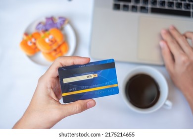 Hand Holding Credit Card For Online Shopping On Laptop During Eating Halloween Cookies And Coffee. Happy Halloween, Hello October, Fall Autumn, Festive, Party And Holiday Concept