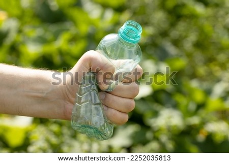 Hand holding crumpled empty plastic bottle in the park
