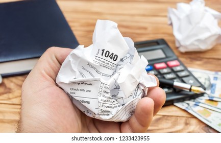 Hand Holding Crumpled Tax Form Over Office Table.