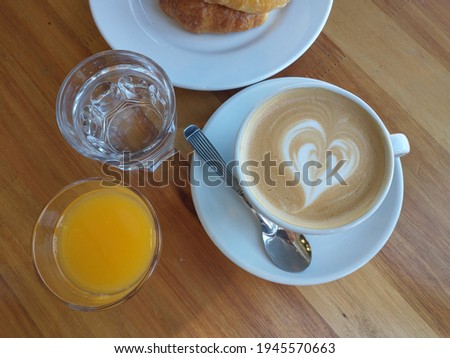 hand holding cup of cabe with milk accompanied by orange juice croissants and water, breakfast in cafe de buenos aires