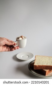 Hand Holding Cup Of Coffee With Marshmallow And Slice Bread On White Background. Morning Breakfast, Coffee Break. Tasty Beverage And Sweet Bakery. Winter And Autumn  Concept