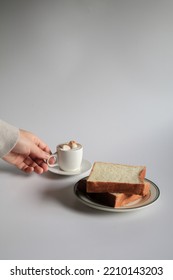 Hand Holding Cup Of Coffee With Marshmallow And Slice Bread On White Background. Morning Breakfast, Coffee Break. Tasty Beverage And Sweet Bakery. Winter And Autumn  Concept