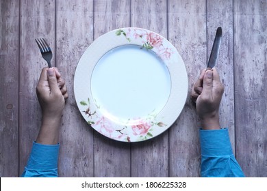 Hand Holding Cutlery And Empty Plate On Wooden Background Top Down