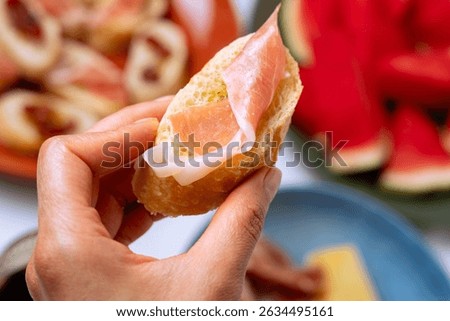Hand holding a delicious slice of bread topped with prosciutto and cheese, ready to be enjoyed