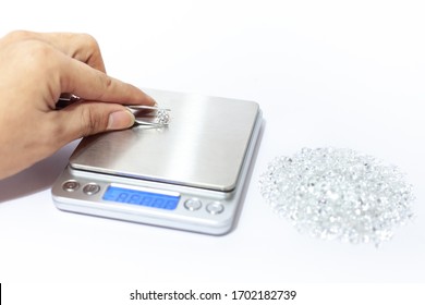 Hand holding a diamond with weight scale, tweezers and a pile of diamond. Worker measures the weight of gems on a jewelry scale isolated on white background.