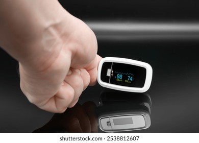 hand holding a digital pulse oximeter, displaying oxygen saturation (SpO2) and heart rate (PR) on a clear screen against a dark background.  - Powered by Shutterstock