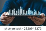 Hand holding a digital tablet with a virtual city skyline hologram. Concept of real estate, smart city, and modern urban technology.