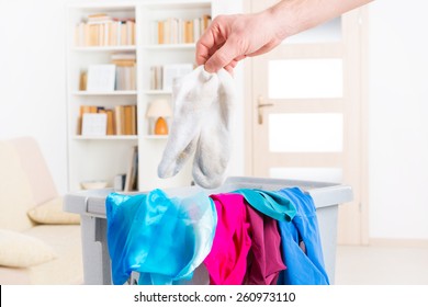 Hand Holding Dirty White Socks Over A Hamper Or Basket