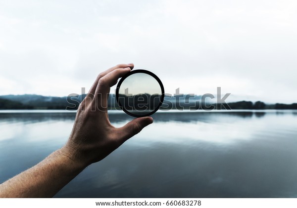 Hand Holding DSLR Camera Lens Filter in Hand\
in Front of River Mountain Nature\
Scene