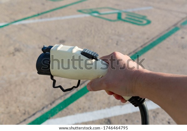 Hand holding Electric car charger.\
Electric Vehicle EV Charging station & Charger. Human hand is\
holding Electric Car Charging connect to Electric\
car.