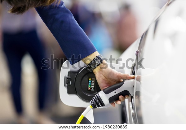 Hand holding Electric car charger. Electric\
Vehicle EV Charging station and Charger. Human hand is holding\
Electric Car Charging connect to Electric\
car.