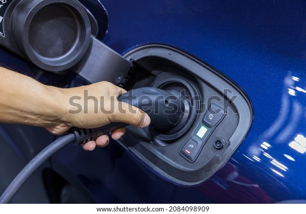 Hand holding Electric car charger. Electric\
Vehicle EV Charging station and Charger. Human hand is holding\
Electric Car Charging connect to Electric\
car.