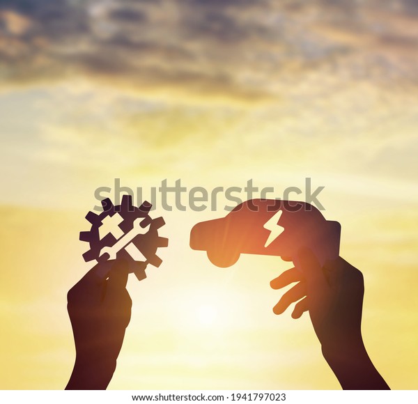 Hand holding electric car icon and holding gear icon\
at sunset sky.