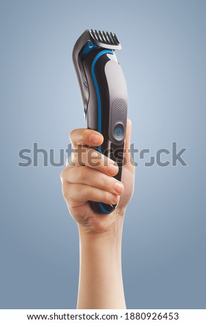 hand holding an electric hair clipper on a blue background