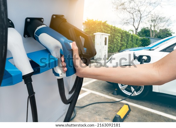 Hand holding electric plug-in charger on blur car\
charging. EV car charging at electric car charging station. EV car\
charging point. Electric vehicle fast charge. Sustainable power.\
Green energy.