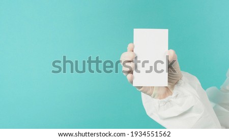Hand holding empty blank white card.Hand with ppe suit, latex glove on green or Tiffany Blue background. Empty space for text
