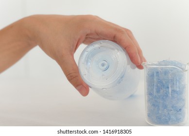 Hand Holding Empty Bottle & Bottle Flake,PET Bottle Flake,Plastic Bottle Crushed,Small Pieces Of Cut Blue Plastic Bottles In Beaker Glass.Chemical Concept