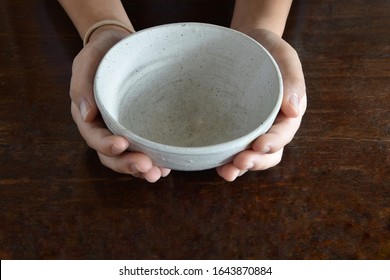 Hand holding empty white bowl on wood table background 