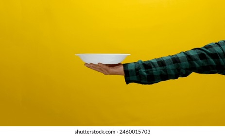 Hand holding empty white plate isolated on a yellow background - Powered by Shutterstock