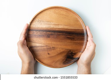 Hand holding empty wooden plate isolated on white, top view.