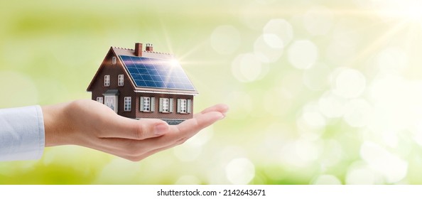 Hand holding an energy efficient model house with solar panels, ecology and sustainability concept - Shutterstock ID 2142643671