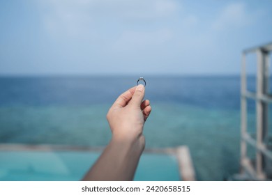 Hand holding engagement ring with ocean view background. - Powered by Shutterstock