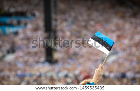 Hand holding Estonian flag over the crowd at estonian folk singing festival, called 'laulupidu' held every 5 years since 150 years ago, possible most important event of the country history