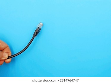 A hand holding an An ethernet cable capable of connecting different devices to the Internet, on a blue background. Space for text - Shutterstock ID 2314964747