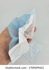 hand holding a face mask been cut into half to show its 3ply layers inside, isolated in white background.
