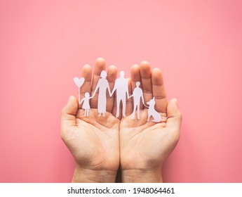 Hand holding family paper cut on pink background. Family day concept, foster care, domestic violence, homeschool, international day of families, world mental health day, world autism awareness day.